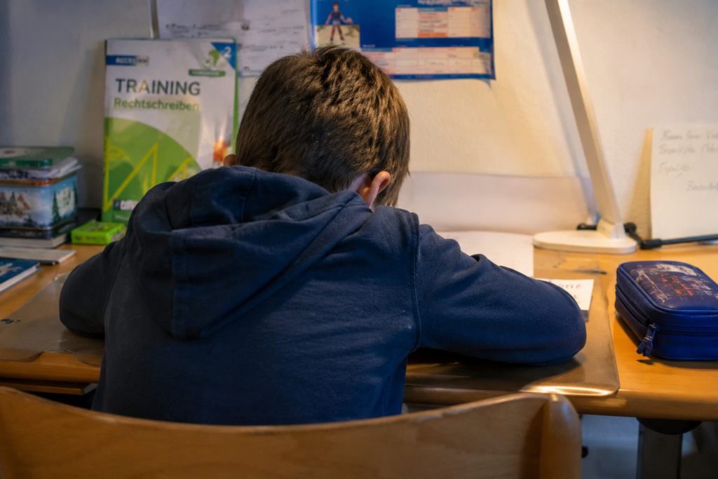 Kind sitzt nachdenklich am Schreibtisch und kämpft mit Lese- und Rechtschreibschwierigkeiten (LRS)